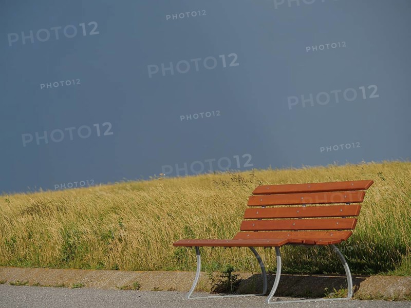 Lonely wooden bench on a grassy field under a dark, cloudy sky, Baltrum Germany