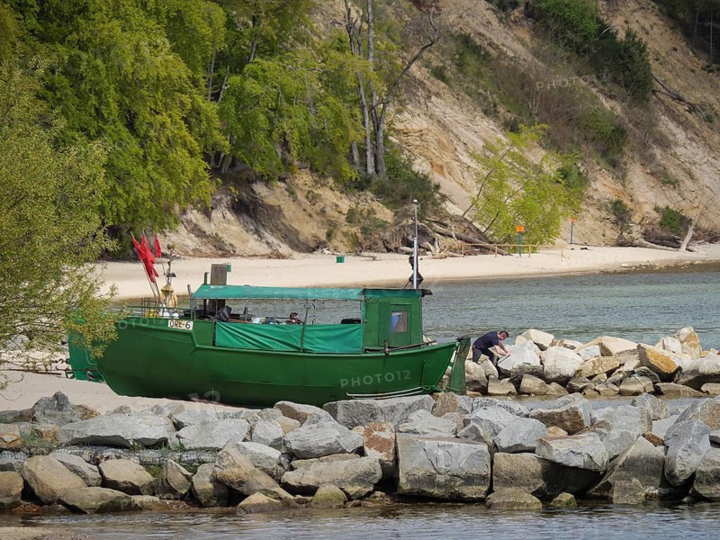 A green boat lies on a rocky shore, in the background dense forest and sandy beach, spring on the Baltic Sea coast with green fishing boats on the beach and green trees on the shore, Sopot, Poland, Europe