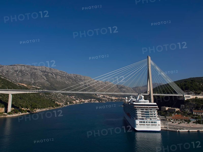 Suspension bridge over a river with a large cruise ship, surrounded by mountains and blue sky, the old town of Dubrovnik with historic houses, churches, red roofs and fortress walls, dubrovnik, coratia