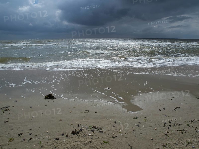 Restless waves on a sandy beach under a cloudy sky. The sea looks impetuous and agitated, view of the wide sea with clouds in the sky, Norderney, Germany, Europe