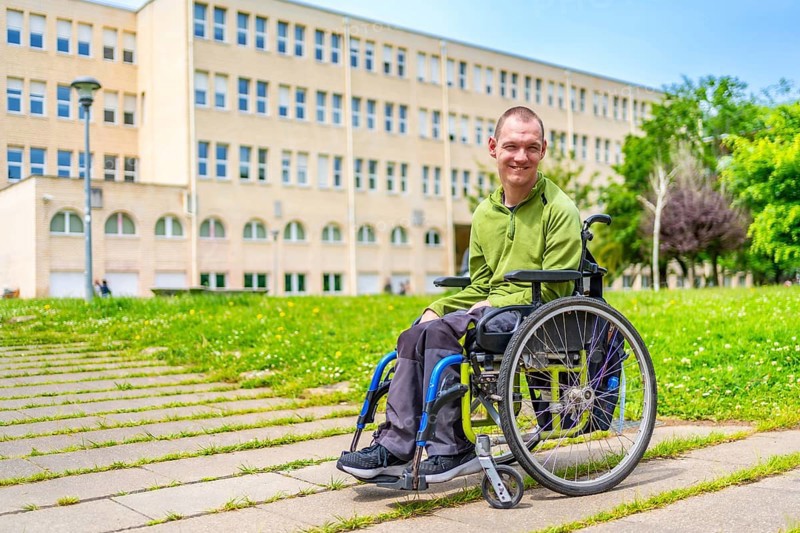 Full length portrait of a caucasian young man with cerebral palsy in wheelchair in the university campus alone