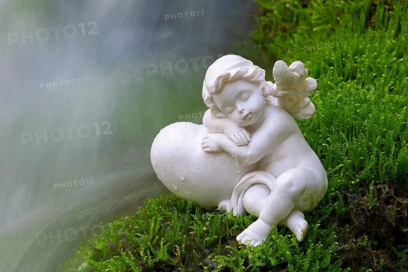 Porcelain angel figurine on moss by a waterfall
