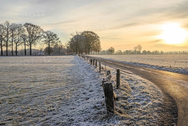 Rural winter landscape at sunrise with icy road and frozen fields, Frosty winter time in the early morning on fields and meadows in Muensterland, velen, Germany, Europe