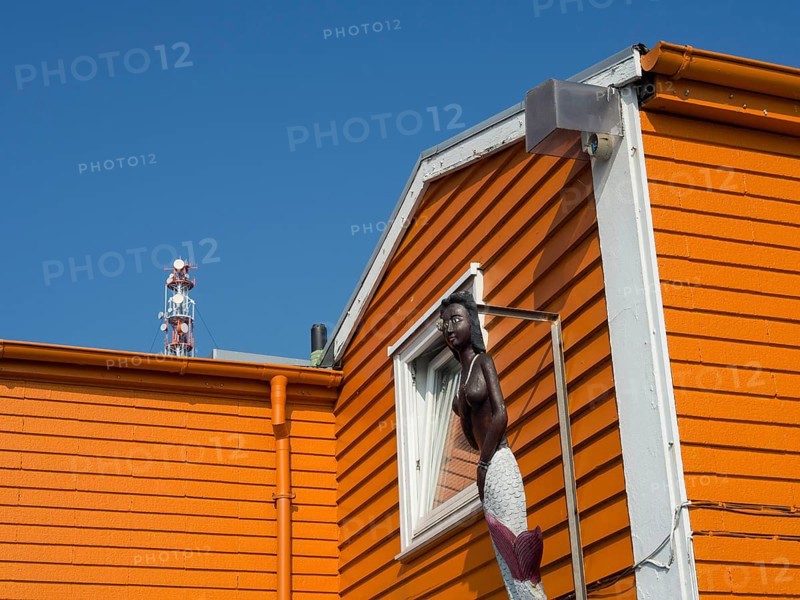 An orange-coloured house wall with a statue of a mermaid in front of a clear blue sky, Heligoland, Germany, Europe