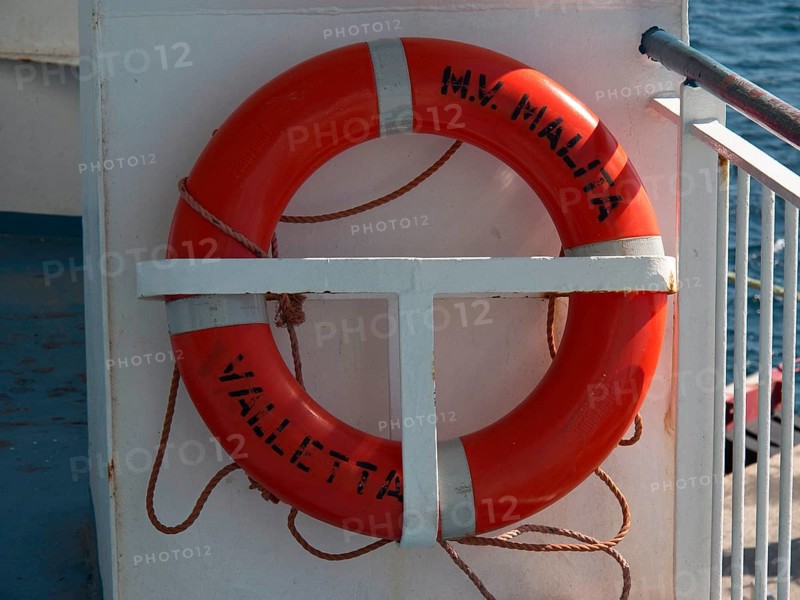 A bright orange lifebuoy with lettering on board a boat, the island of Gozo with historic houses, colourful balconies, magnificent churches and boats in the harbour, Gozo, Malta, Europe