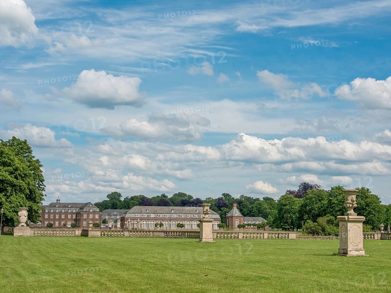 Sweeping view of a historic building, corridor of sculptures and green lawn, under an open sky with clouds, historic castle with a green park with sculptures and paths, nordkirchen, germany