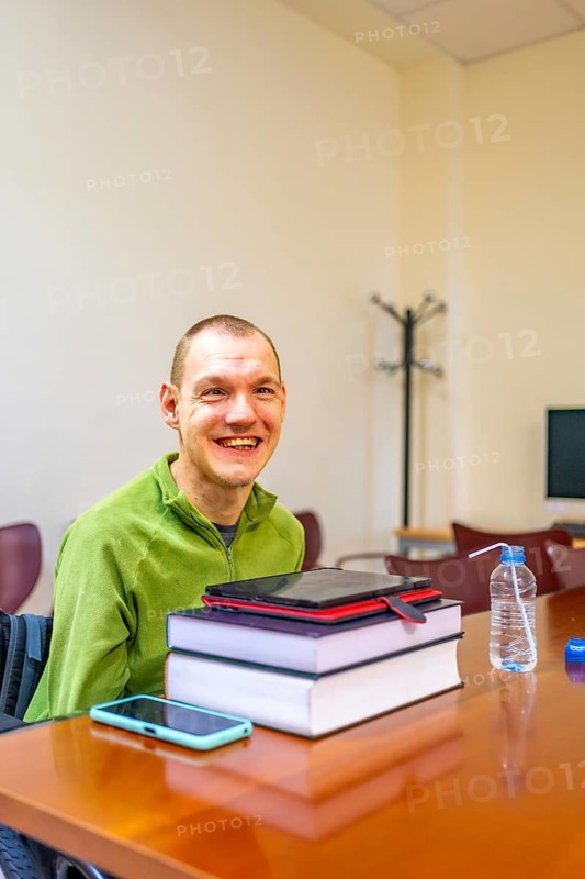 Vertical photo with concept of technology helping a man with disability to study in the university using digital tablet and mobile sitting on wheelchair