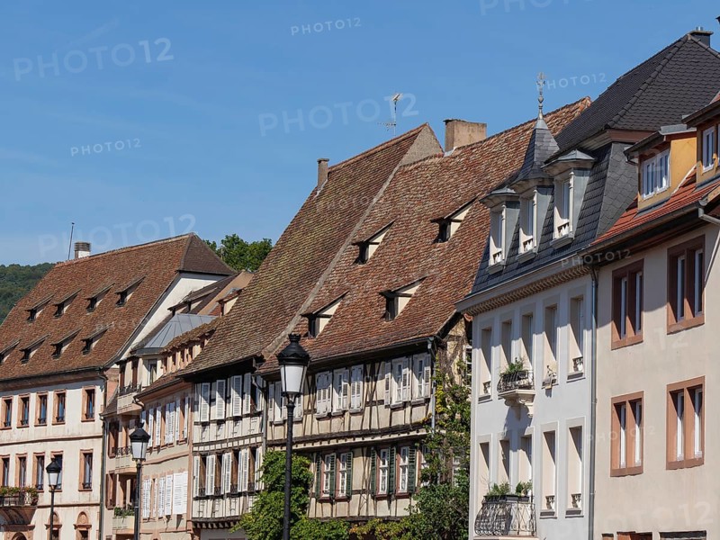 Historic half-timbered houses with red roof tiles and shutters under a blue sky, historic house fronts and a large church in Alsace, Wissembourg, France, Europe