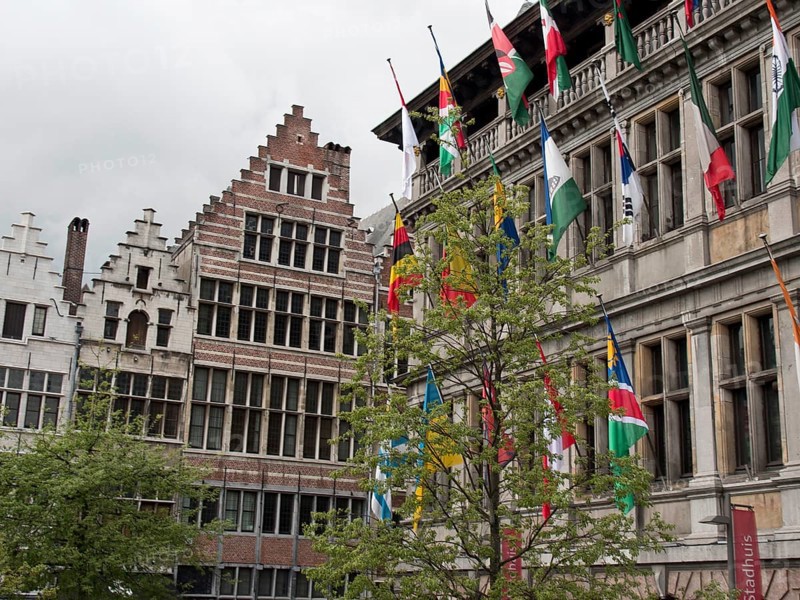 Historic buildings with ornate gables and many flags, trees in front under a gloomy sky, Historic buildings, Antwerp, Belgium, Europe