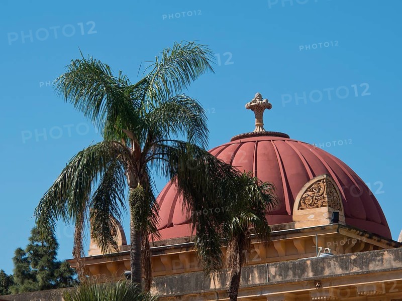 Historic building with red dome behind palm trees in front of a bright blue sky, palermo in sicily with an impressive cathedral, monuments and old houses with balconies, palm trees and flowers in italy, palermo, sicily