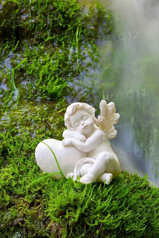 Porcelain angel figurine on moss by a waterfall