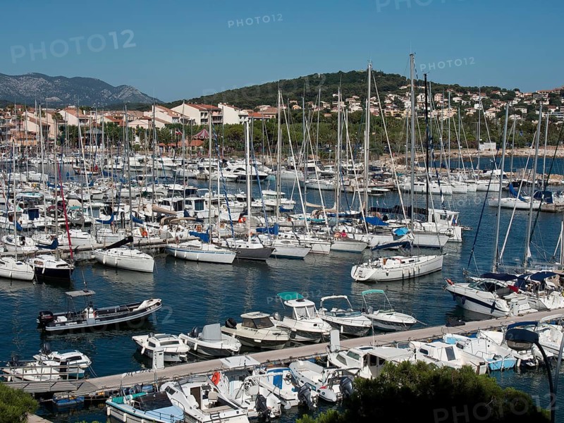 A busy marina full of sailboats and yachts, with a town and hills in the background, la seyne sur mer on the mediterranean sea with boats in the harbour, trees and houses on the coast, la seyne sur mer, france