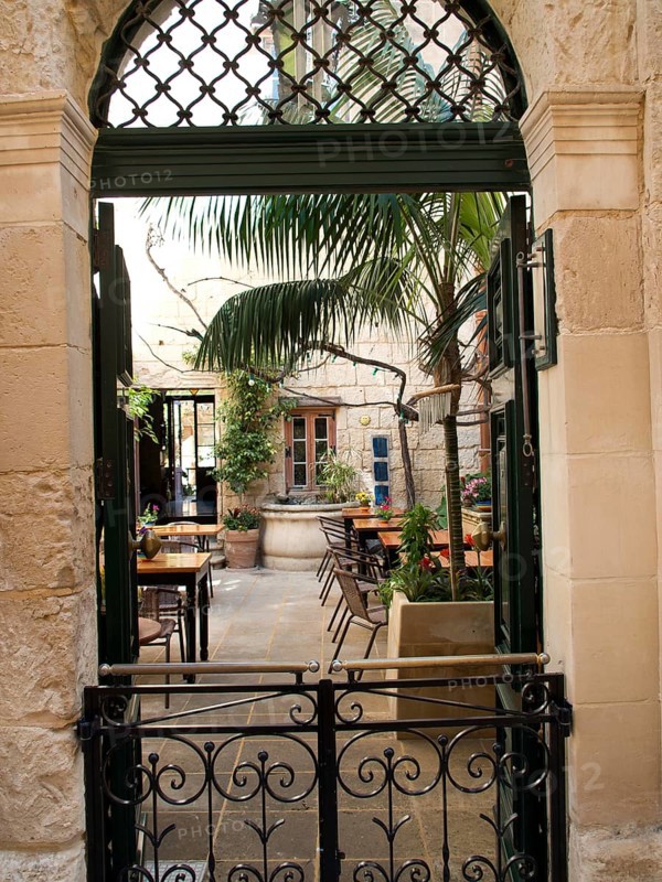 An inviting inner courtyard with palm trees is accessible through an iron gate, the town of mdina on the island of malta with historic houses, colourful balconies, magnificent churches, mdina, Malta, Europe