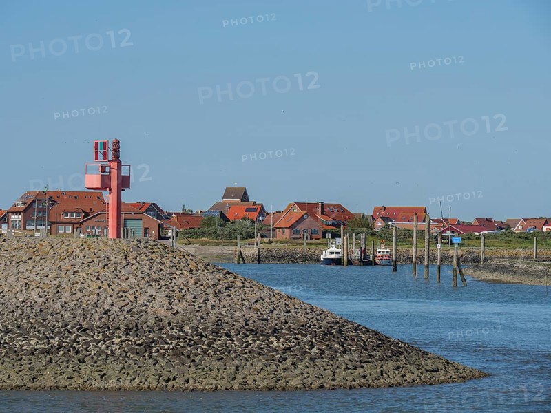 A harbour with red houses and boats moored on the shore, with a clear blue sky, Baltrum Germany