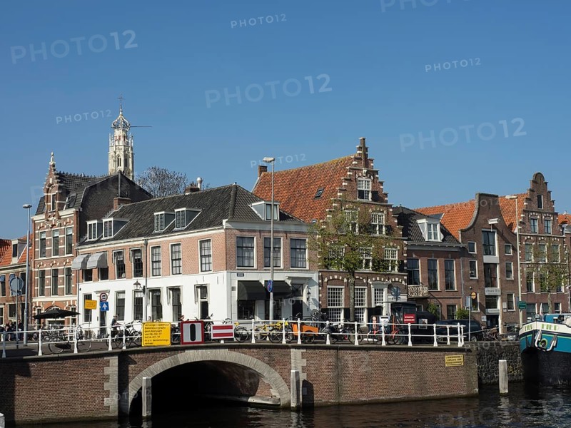 Historic buildings along a river with bridge and boats under a blue sky, Haarlem, Netherlands
