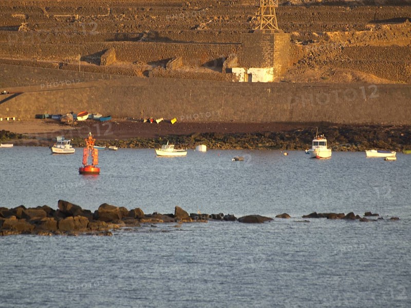 Boats and buoys on the sea in front of a rocky coastline at sunset, Lanzarote with a hisotric fortress and lava mountains, Lanzarote, Spain, Europe