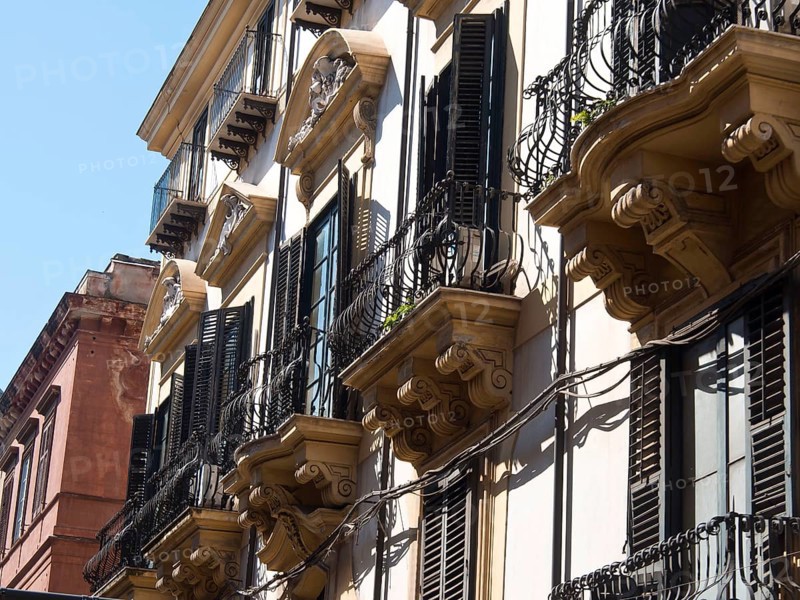 Historic buildings with wrought iron balconies and black shutters in a sunny European city, palermo in sicily with an impressive cathedral, monuments and old houses with balconies, palm trees and flowers in italy, palermo, sicily