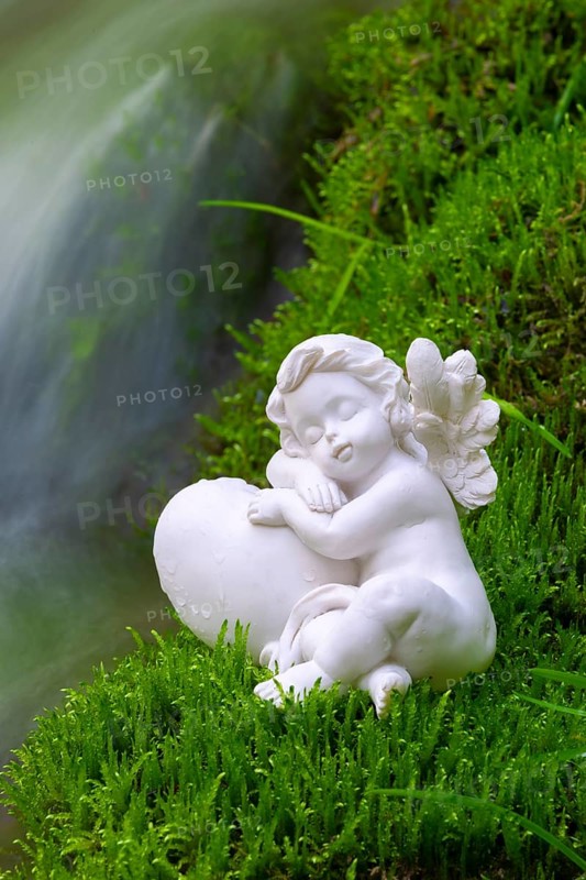 Porcelain angel figurine on moss by a waterfall