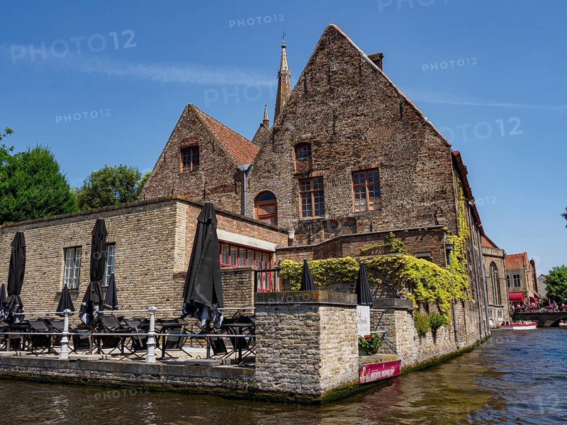 Historic building on the canal in Bruges with a cafe and blue sky on a sunny day, historic houses and churches with towers on a river in Belgium, Bruges, Belgium, Europe