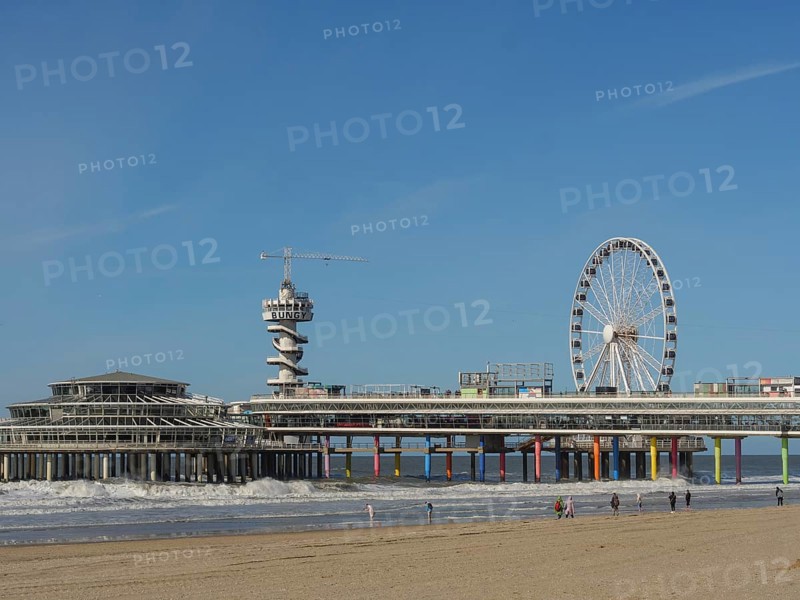 Pier with Ferris wheel and tower on the beach, people walking along the beach, parasols and a pier on the beach of Scheveningen, scheveningen, Netherlands