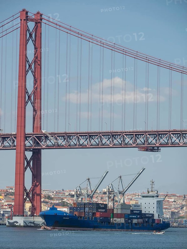 Red suspension bridge over the water, below container harbour with large cargo ships, Lisbon, Portugal, Europe