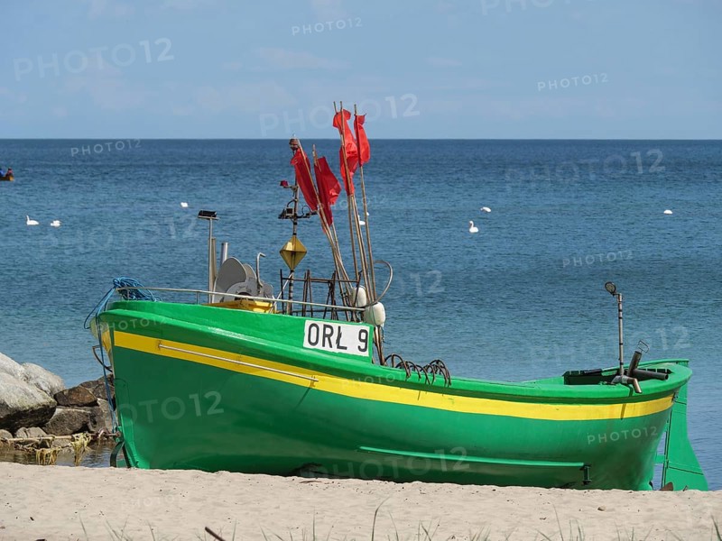 A green boat with red flags stands on the beach, propped up on the sand, in front of a calm sea, green and yellow fishing boats on the beach in Poland, sopot, poland