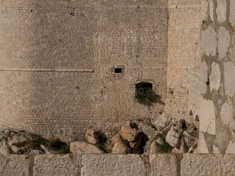 Close-up of a medieval stone wall and fortress with neighbouring rocks, the old town of Dubrovnik with historic houses, churches, red roofs and fortress walls, dubrovnik, coratia
