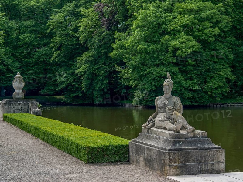 Stone statue in a park next to a lake, surrounded by dense green trees, historic castle with a green park with sculptures and paths, nordkirchen, germany