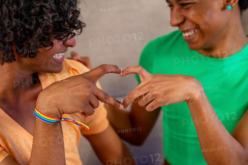 Close-up of gay couple join hands forming heart shape sitting on the sofa at home