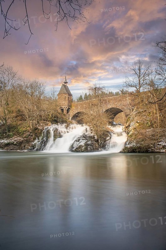 Beautiful landscape in winter with ice and snow. Waterfall of the river Elz near the castle Pyrmont, the country inn Pyrmonter Muehle directly at a lake. A historic bridge in Rhineland-Palatinate, Germany, Europe