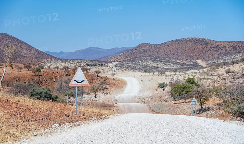 Road with road sign Attention river crossing, gravel track leads through barren dry landscape with red and yellow hills, Kaokoveld, Kunene, Namibia, Africa