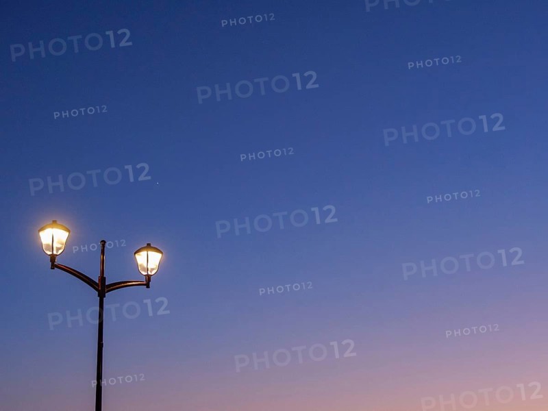 A street lamp shines against a dark blue sky at dusk, sunset in many colours on a beach with a calm sea, de haan, belgium