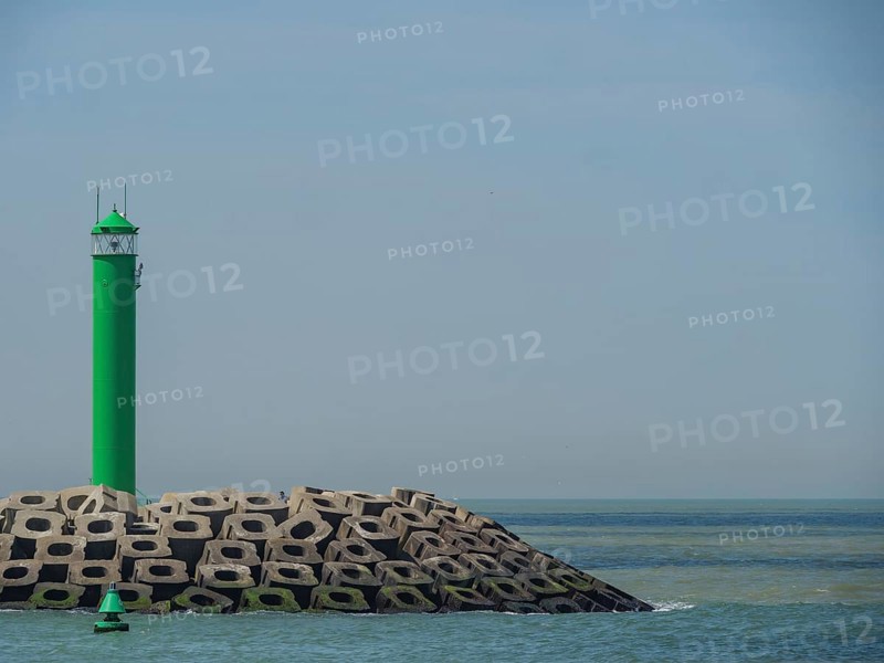 A single green lighthouse next to concrete breakwaters with calm sea in the background, lighthouses at a harbour entrance by the sea in Belgium against a blue sky, oostende, Belgium, Europe