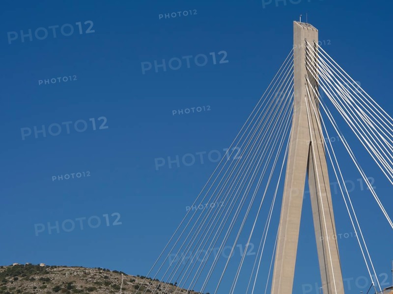 Detailed view of a modern cable bridge in front of a cloudless blue sky, the old town of Dubrovnik with historic houses, churches, red roofs and fortress walls, dubrovnik, coratia