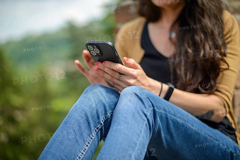 Young woman in casual clothing focused on conversation with smartphone in a peaceful garden with blurred brickwork in the foreground