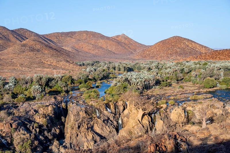 Kunene River with green vegetation in dry red mountain landscape, waterfall and African Baobab (Adansonia digitata), in the evening light, Epupa Falls, Kunene, Namibia, Africa