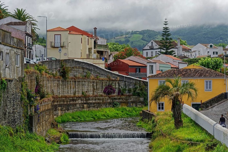 An idyllic village with colourfully painted houses, through which the Ribeira Grande river flows, surrounded by green hills and a cloudy atmosphere, coastal town of Ribeira Grande, Santa Barbara, Sao Miguel, Azores, Portugal, Europe