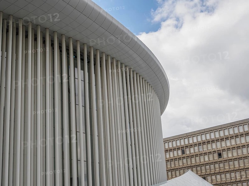 Part of a modern building in Luxembourg with vertical columns and a slightly cloudy sky in the background, modern buildings with trees and glass facades, luxembourg