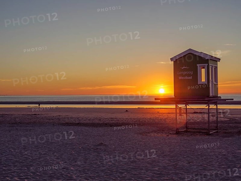 Beach at sunset with a raised lifeguard tower and a wide view of the sea and sky, setting sun on the North Sea beach with warm light over colourful beach chairs, langeoog, germany