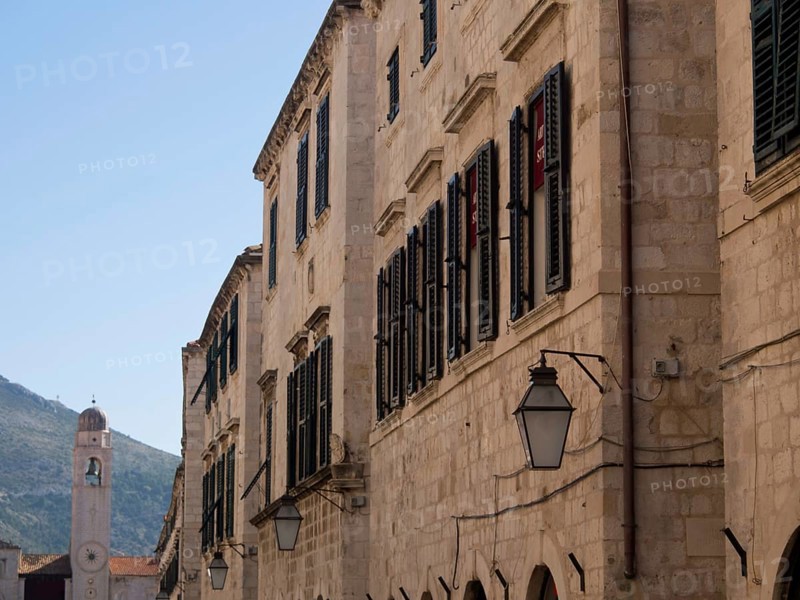 Historic stone buildings with shutters and street lamps in an old town under a bright blue sky, the old town of Dubrovnik with historic houses, churches, red roofs and fortress walls, dubrovnik, coratia