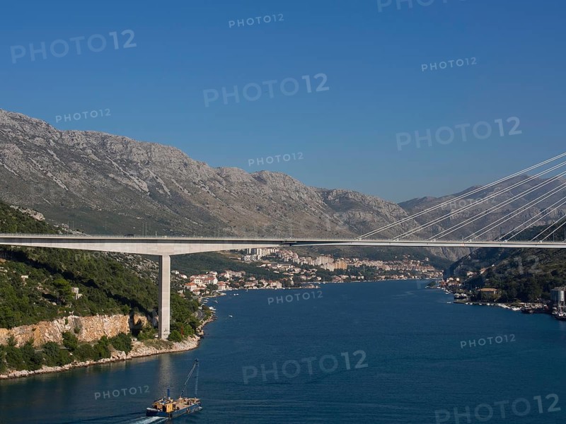Wide view of a suspension bridge over a wide river, surrounded by a city and mountains under a clear sky, the old town of Dubrovnik with historic houses, churches, red roofs and fortress walls, dubrovnik, coratia