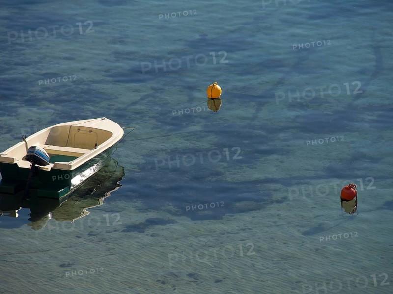 A small boat floats on clear water surrounded by buoys that are reflected in the water, the old town of Dubrovnik with historic houses, churches, red roofs and fortress walls, dubrovnik, coratia