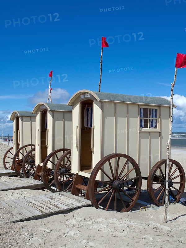 Three beige changing cabins with large wooden wheels on a beach under a blue sky with clouds, historic bathing carts on a sandy beach in front of a blue sky, Norderney, Germany, Europe