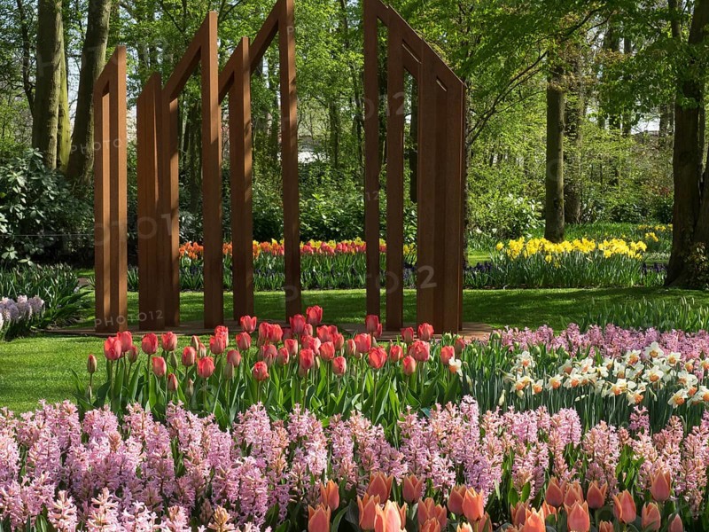 A colourful flower bed with tulips and hyacinths in a spring-like forest with a sculpture in the background, many colourful, blooming tulips in a garden in the Netherlands for the Springtime Zeti, Amsterdam, Netherlands