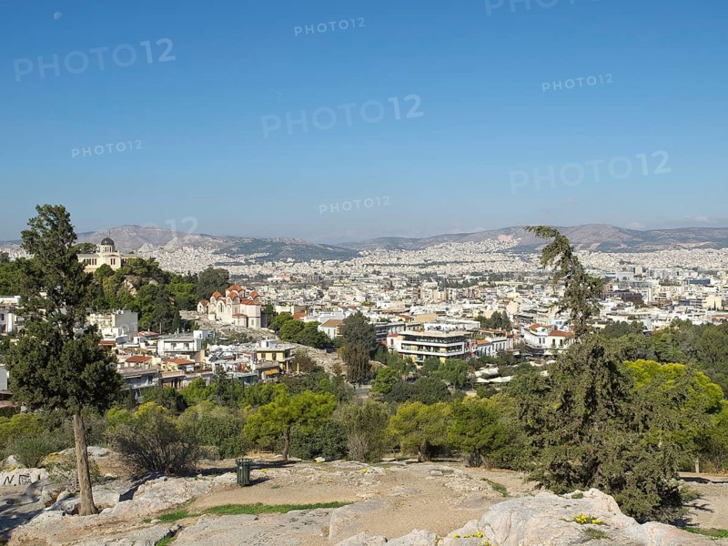 City view from a hill surrounded by buildings and trees, Ancient buildings with columns and trees on the Acropolis in Athens against a blue sky, athens, greece