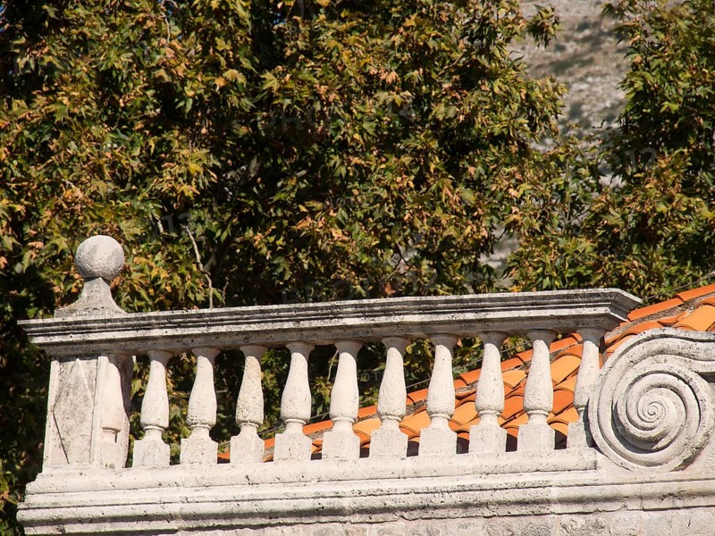 Close-up of a stone balcony balustrade with decorative ornaments and autumnal trees in the background, the old town of Dubrovnik with historic houses, churches, red roofs and fortress walls, dubrovnik, coratia