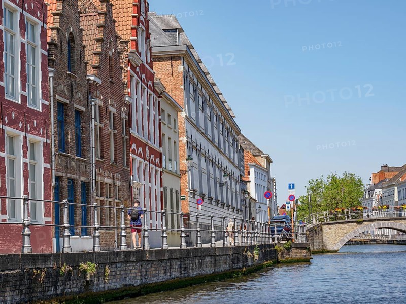 Historic brick buildings along a canal on a sunny day with people strolling quietly, historic city by the river with ornate gables, old facades and historic towers, Bruges, Belgium, Europe