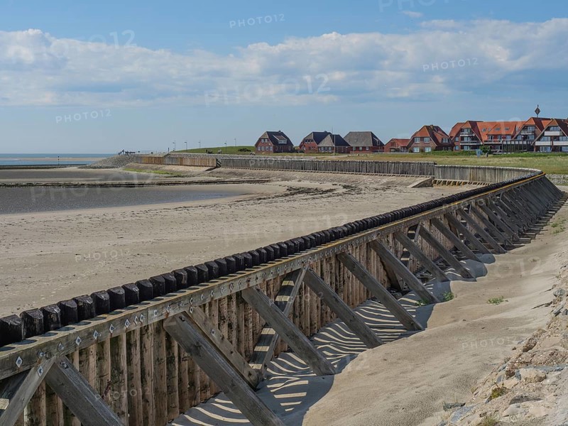 A beach with wooden constructions and houses in the background, sea and sky with some clouds, Baltrum Germany