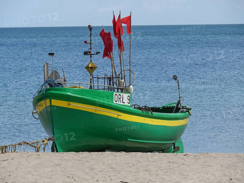 Green boat with red flags standing on sandy beach in front of calm sea under blue sky, green and yellow fishing boats on the beach in Poland, sopot, poland
