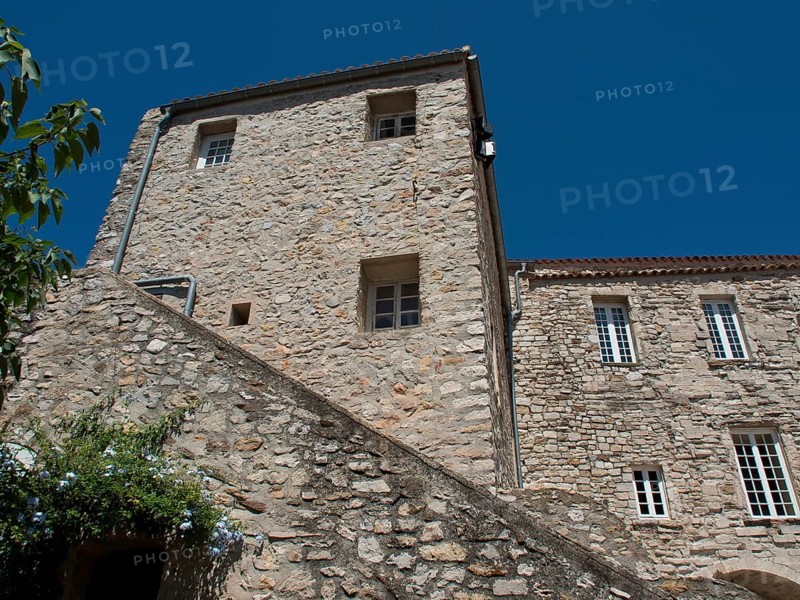 A historic building with stone walls and multiple windows under a clear blue sky, architectural details clearly visible, historic stone houses overgrown with greenery in Provence, Le Castellet, France, Europe